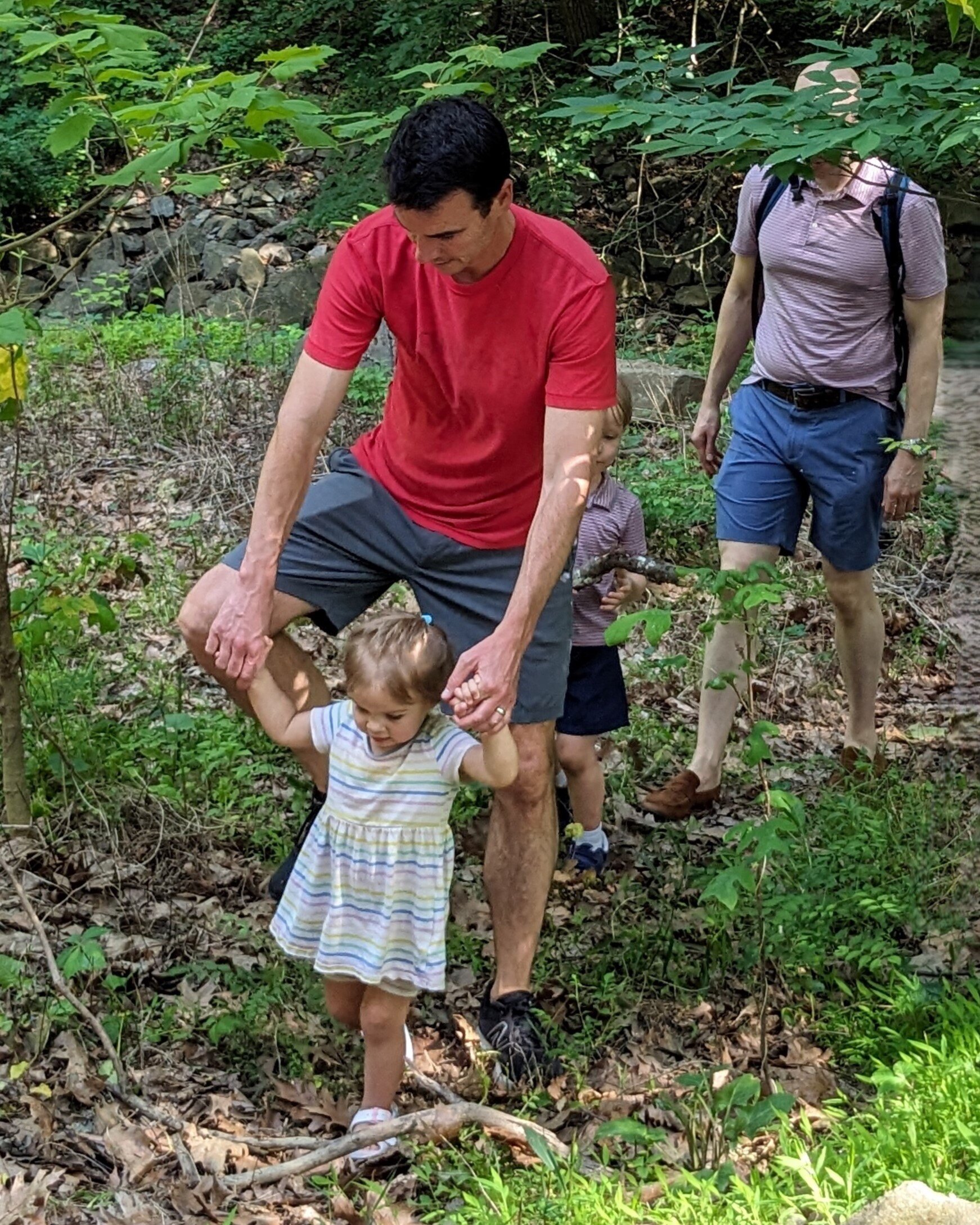 adult holding child's hands as they walk through the woods